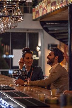 a man and woman sitting at a bar with wine glasses in their hands, smiling