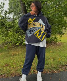 a woman standing in front of some trees wearing a sweatshirt and sweatpants with the word michigan on it