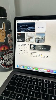 an open laptop computer sitting on top of a white desk next to a black bottle