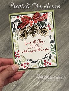 a hand holding up a christmas card with pine cones and holly berries on the front