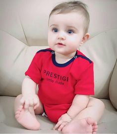 a little boy sitting on top of a couch wearing a red shirt and blue pants