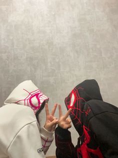 two people in hoodies making the peace sign with their hands while wearing spider - man costumes