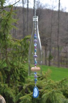 a glass bottle with beads hanging from it's side in front of some trees