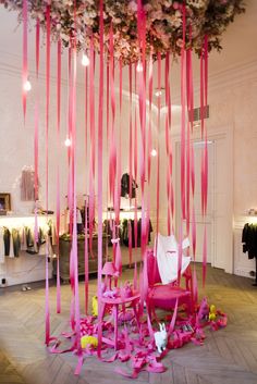 a room with pink ribbons hanging from the ceiling and chairs on the floor in front of it