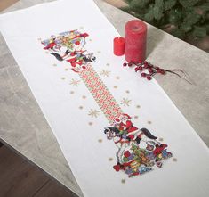 a cross stitch table runner with mickey and minnie on it, next to a candle