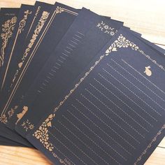 five black cards with gold designs on them sitting on a wooden table next to each other