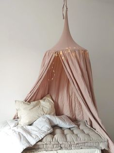 a bed with a pink canopy over it and pillows on the bottom floor, in front of a white wall