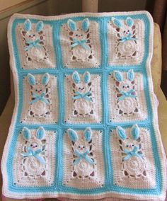 a blue and white crocheted baby blanket on top of a table next to a window