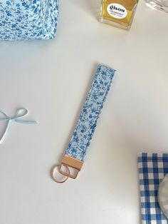 a blue and white flowered fabric keychain next to a bottle of perfume