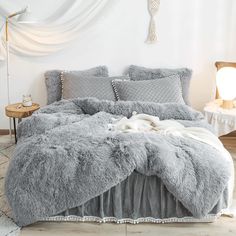 a bed with grey comforter and pillows in a white room next to a table