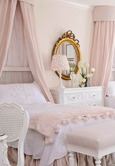 a white bed sitting under a mirror next to a table with flowers on top of it