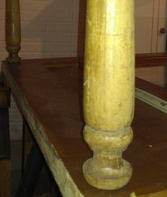 an old wooden table with a large yellow vase on it's top and two candles in the background