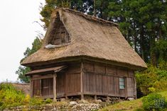 an old wooden house with a thatched roof and stone walls in front of trees