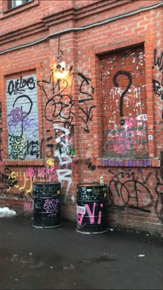 graffiti is spray painted on the side of an old brick building with three black trash cans in front of it