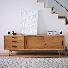 a wooden dresser sitting in front of a stair case next to a book shelf and white wall