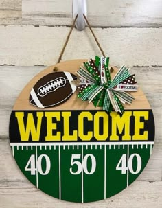 a welcome sign hanging on the side of a wooden wall with footballs and bows