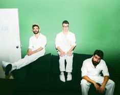 three men sitting on a couch in front of a green wall