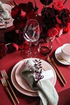 a table set with red flowers and place settings