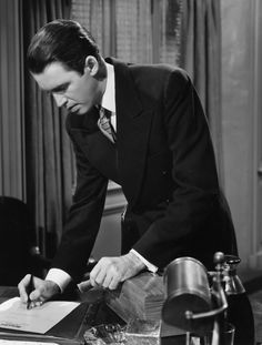 a man in a suit writing on a piece of paper while sitting at a desk