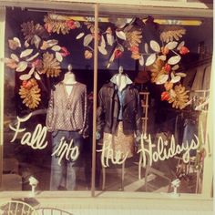 two mannequins in front of a store window with fall decorations on it