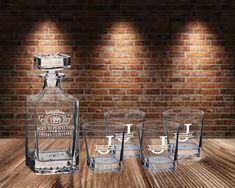 three shot glasses and an empty bottle on a wooden table in front of a brick wall