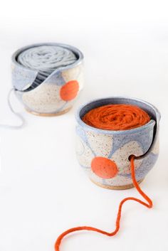 two bowls with orange yarn in them sitting on a white surface next to each other