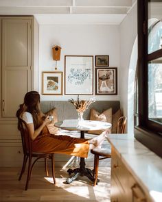 a woman sitting at a table in front of a window with pictures on the wall