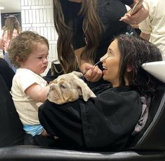 a woman sitting in a chair with a small dog on her lap while she brushes her teeth