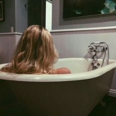 a woman is sitting in the bathtub with her long hair blowing back and looking into the mirror