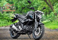 a black motorcycle parked on the side of a road next to some green trees and bushes