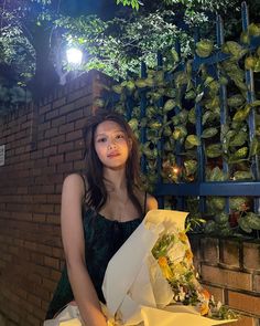 a young woman is holding a bunch of flowers in front of a brick wall at night