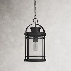 a light hanging from a chain on a white wall with a black caged light fixture