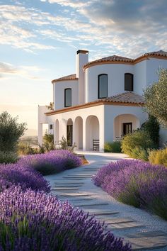 a white house with purple flowers in the foreground and lavender bushes on the other side