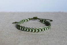 a green and white braided bracelet sitting on top of a cloth covered tablecloth