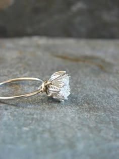 a close up of a ring with a flower on the end and a stone surface in the background