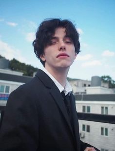 a young man in a suit and tie standing on a balcony looking off into the distance