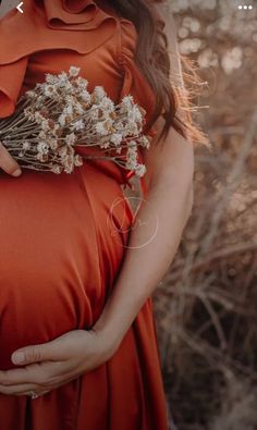 a pregnant woman in an orange dress is holding her belly with flowers growing out of it