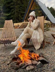 a woman sitting in front of a campfire with her feet up on the ground