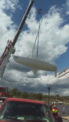 a red car is parked in front of a crane with a boat on it's back