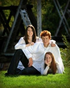 two people sitting on the ground in front of a metal bridge and grass with trees behind them