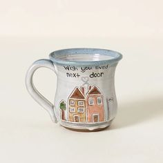 a ceramic mug with words written on the side and houses painted on the inside, sitting on a white surface