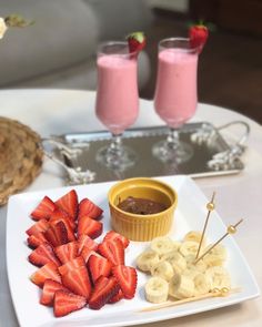 strawberries and bananas on a white plate with two glasses of pink smoothie in the background