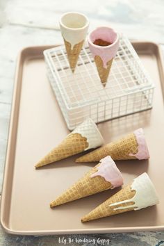 four ice cream cones with pink icing on a tray next to a small cup