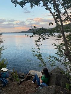 a woman sitting on top of a rock next to a body of water