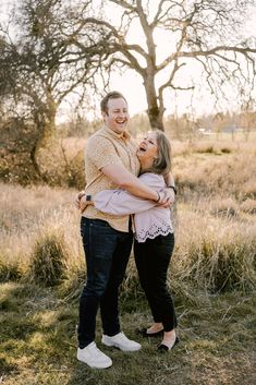 an engaged couple hugging in front of a tree