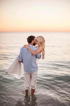 a man and woman standing in the water at sunset with their arms around each other