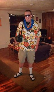 a man standing in a living room wearing sunglasses and a flowered shirt with a camera on his neck