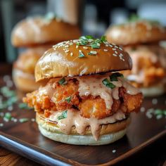 two chicken burgers with sauce and cheese on a wooden tray next to some bread buns