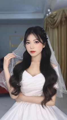 a woman in a white dress with long hair and veil on her head is posing for the camera