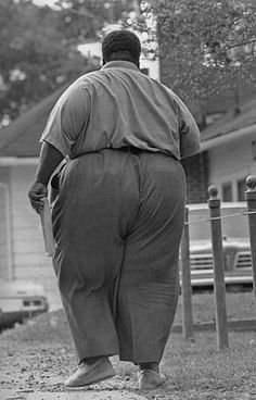 a man walking down the street with his back turned to the camera, in front of a house